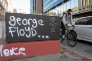 A man rides his bicycle  in Oakland, CA, on May 30, 2020, by wood boards with graffiti in support of  George Floyd in Minneapolis, MN, who passed away while pleading with arresting officers that he couldn't breathe as one of the officers was shown on video kneeling on his neck.